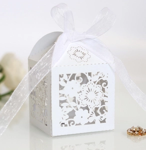 Close-up of white laser-cut wedding favor box with floral patterns and a silk ribbon