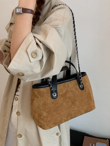 Brown suede crossbody bucket bag with black leather trim and chain strap on khaki coat
