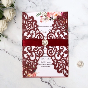 Close-up of laser-cut wedding invitation with burgundy shell, ribbon and rhinestone buckle