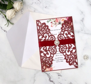 Detail of burgundy laser cut wedding invitation with ribbon and rhinestone buckle