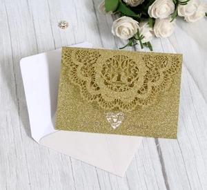 Detail of laser-cut glitter gold wedding invitation with lace patterns and white envelope