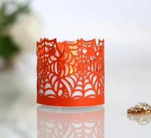 Close-up of orange Halloween spider web laser-cut paper lampshade over LED candle light