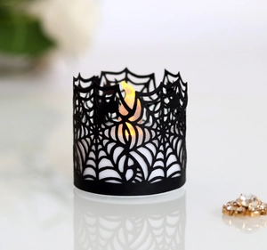 Detail of laser-cut black spider web paper lampshade over warm LED tea light candle