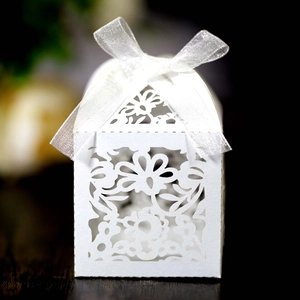 Detail of laser-cut white wedding favor box with floral patterns and a silk ribbon bow