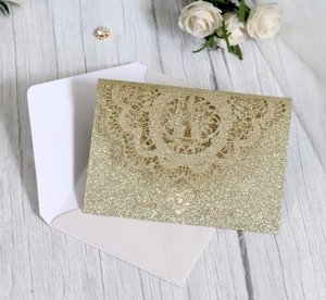 Detail of champagne gold glitter laser-cut wedding invitation with lace pattern and envelope