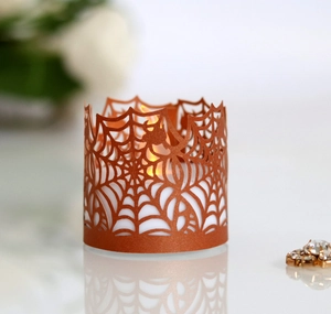 Detailed laser-cut spider web candle sleeve in bright orange for Halloween atmosphere