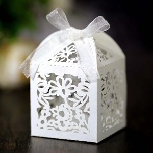 Detailed laser-cut floral pattern on white wedding favor box with a satin ribbon bow