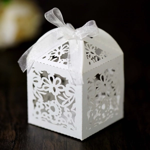 Detail shot of laser-cut white wedding favor box with floral patterns and organza ribbon