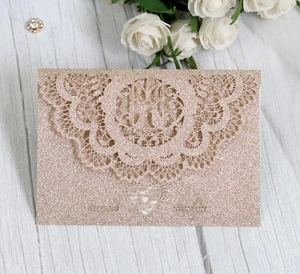 Detail of laser-cut glitter wedding invitation with elegant lace pattern and champagne gold finish
