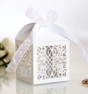 Detail of white laser cut favor box with elegant floral patterns and a satin ribbon bow