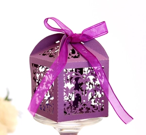 Detail of purple laser-cut wedding favor box with intricate hollow pattern and silk ribbon