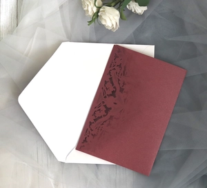 Macro detail of laser-cut floral pattern on burgundy wedding invitation card cover