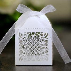 Detail of white laser-cut wedding favor box with elegant floral patterns and ribbon