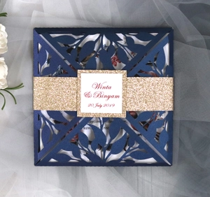 Macro detail of navy blue laser-cut wedding invitation with lace leaf patterns and gold belt