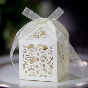Macro detail of white laser-cut wedding favor box with floral patterns and organza ribbon