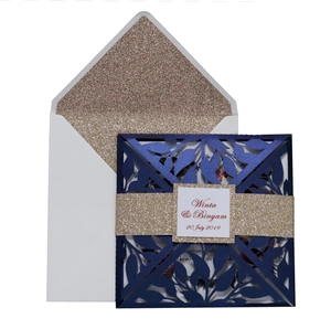 Macro detail of laser cut leaf patterns on navy blue wedding invitation with gold glitter band