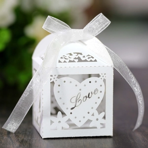 Close-up of white laser-cut wedding favor box with Love heart design and white ribbon bow