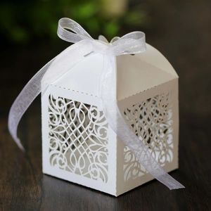 Close-up of white laser-cut favor box with European floral pattern and silk ribbon bow