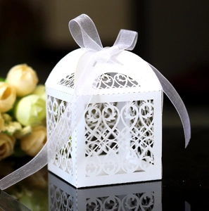Detail of white laser-cut favor box with elegant floral patterns and a silk ribbon bow