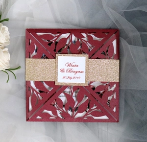 Detail of laser-cut burgundy invitation pocket with gold glitter band and custom tag