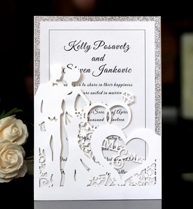 Laser-cut wedding invitation detail featuring a kissing couple and silver glitter border