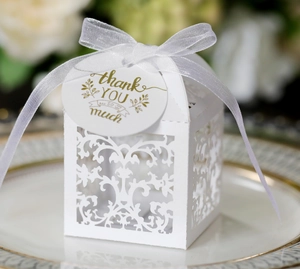 Detailed laser-cut white wedding favor box with vine patterns and gold thank you tag