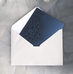 Detail of laser-cut navy lace invitation card with elegant cream envelope on soft tulle