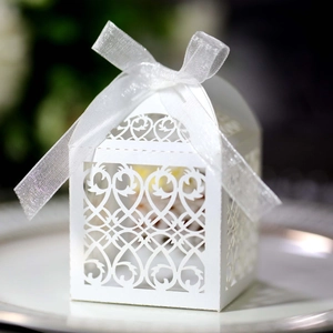 Detail of white laser-cut wedding favor box with ornate hollow patterns and a ribbon bow