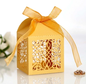 Golden laser-cut hollow gift box with elegant organza ribbon bow on reflective surface