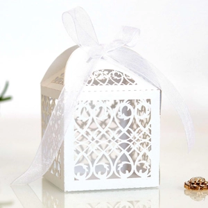 Close-up of white laser-cut wedding favor box with ornate heart patterns and silk ribbon