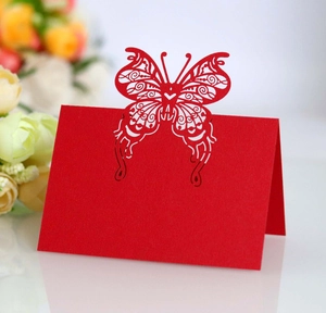 Detail showing intricate laser-cut butterfly pattern on red paper wedding table card