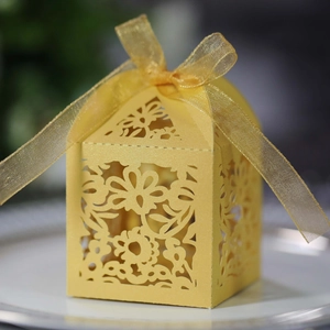 Detail of yellow laser-cut wedding favor box with intricate floral patterns and ribbon bow