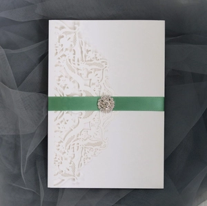 Detail of laser-cut wedding invitation with green silk ribbon and rhinestone buckle