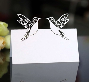 Detail of laser-cut white hummingbird place cards with elegant hollow wing patterns