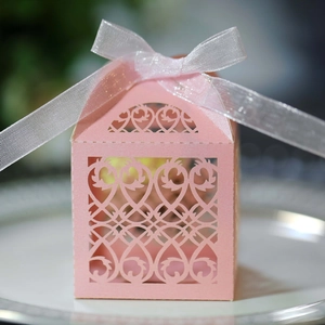 Detail of pink laser-cut wedding favor box with floral patterns and a white ribbon bow