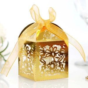 Close-up of laser-cut gold wedding favor box with floral patterns and yellow organza ribbon