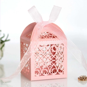 Detail of pink laser-cut favor box with intricate floral patterns and silk ribbon bow
