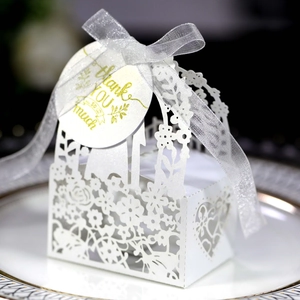 Detail of laser-cut white wedding favor box with floral patterns and a gold thank you tag