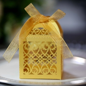 Macro shot of gold laser-cut wedding favor box with intricate hollow pattern and ribbon