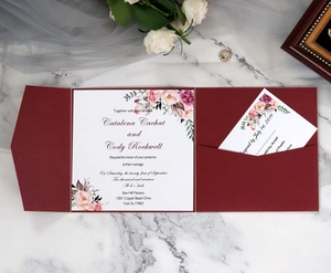 Detail of burgundy pocket wedding invitation set with floral cards on marble surface