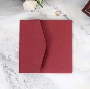 Deep burgundy square envelope with a V-flap design on white marble surface with flowers