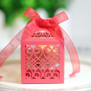 Macro shot of laser-cut red wedding favor box with ribbon on decorative white plate