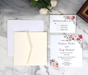 Detail of ivory paper wedding invitation set with pink floral patterns on marble surface