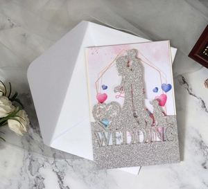 Macro shot of silver glitter laser-cut wedding invitation with couple and dog silhouette