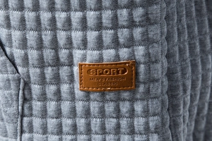 Detail of grey quilted hoodie fabric with 3D waffle texture and brown sport leather label