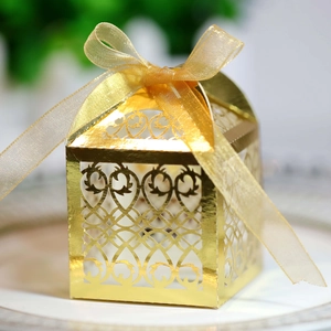 Close-up of golden laser-cut wedding favor box with heart patterns and satin ribbon bow