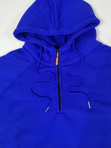 Détail d'un sweat à capuche bleu roi avec fermeture demi-zip et tirette contrastée