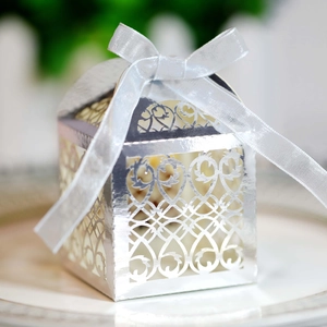 Macro shot of silver laser-cut wedding favor box with ribbon on white porcelain plate