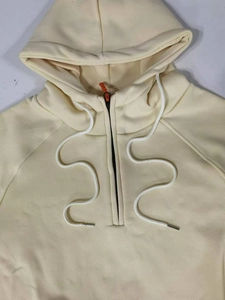Détail du sweat à capuche crème avec cordons blancs et tirette de fermeture orange