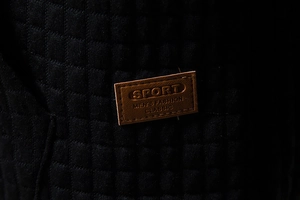 Detail of black quilted fabric and brown embossed leather patch with sport lettering